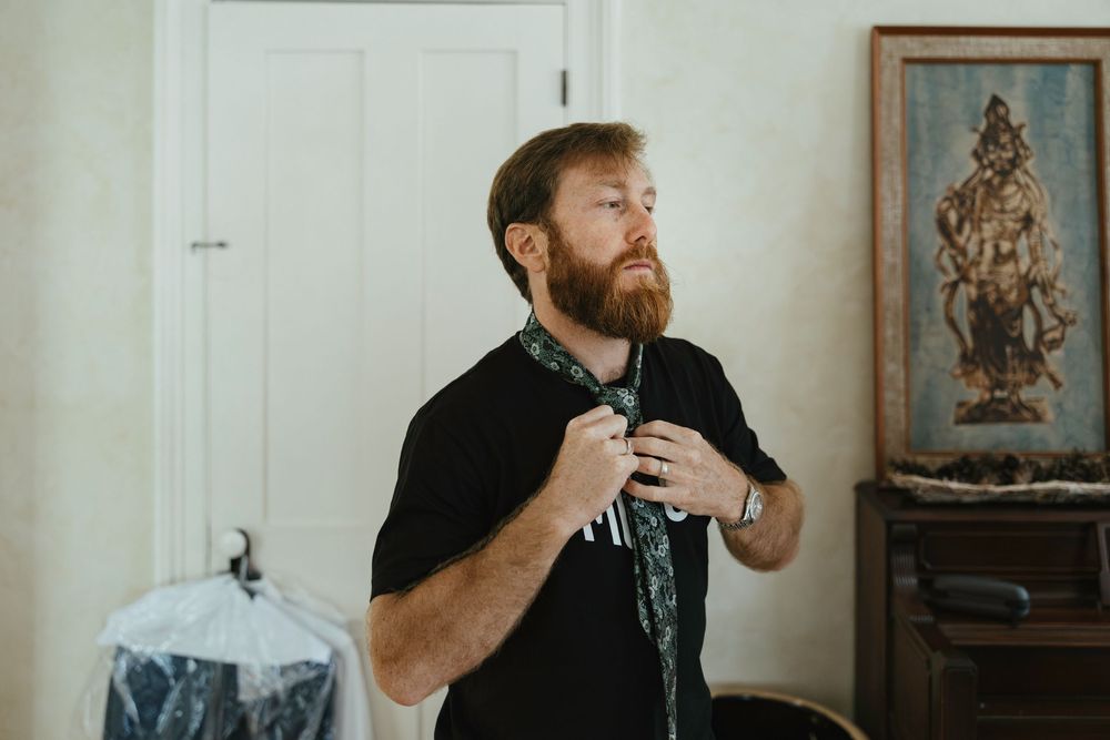 Someone adjusts their black t-shirt while standing in a room with white walls and framed artwork.
