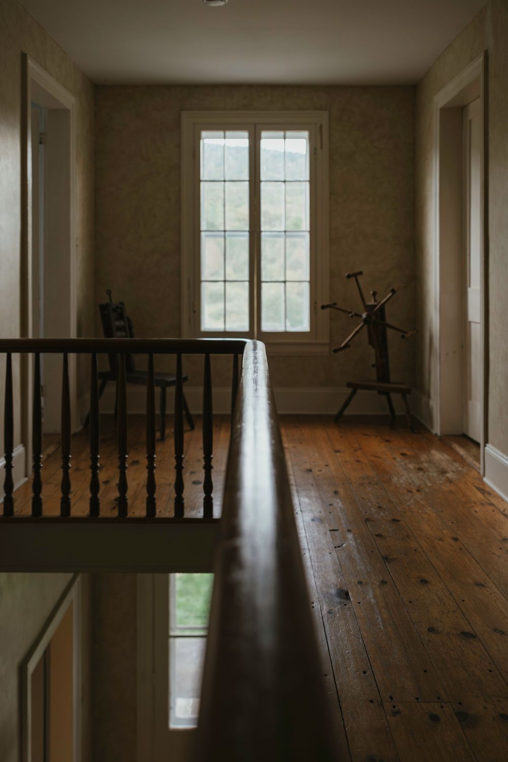 Rustic hallway with wooden floors, tall window, and dark railing features natural light and minimalist decor.