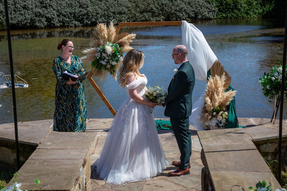 Bride and groom exchanging vows on a waterside platform decorated with pampas grass arch.