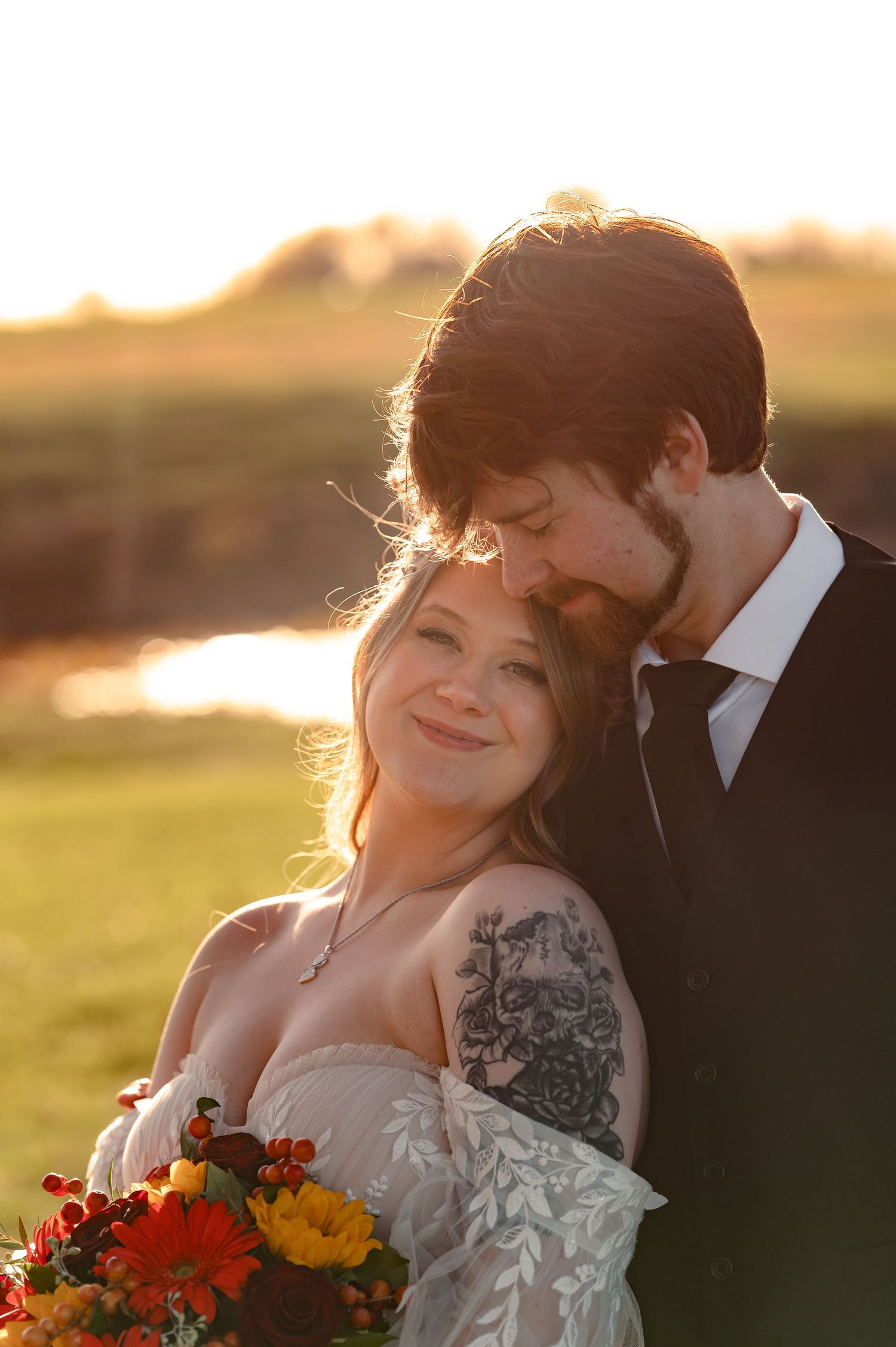 A romantic sunset wedding photoshoot featuring a couple with a vibrant autumn bouquet of red and orange flowers.