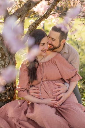 Couple enceinte enlacé sous les cerisiers en fleurs dans une lumière naturelle dorée