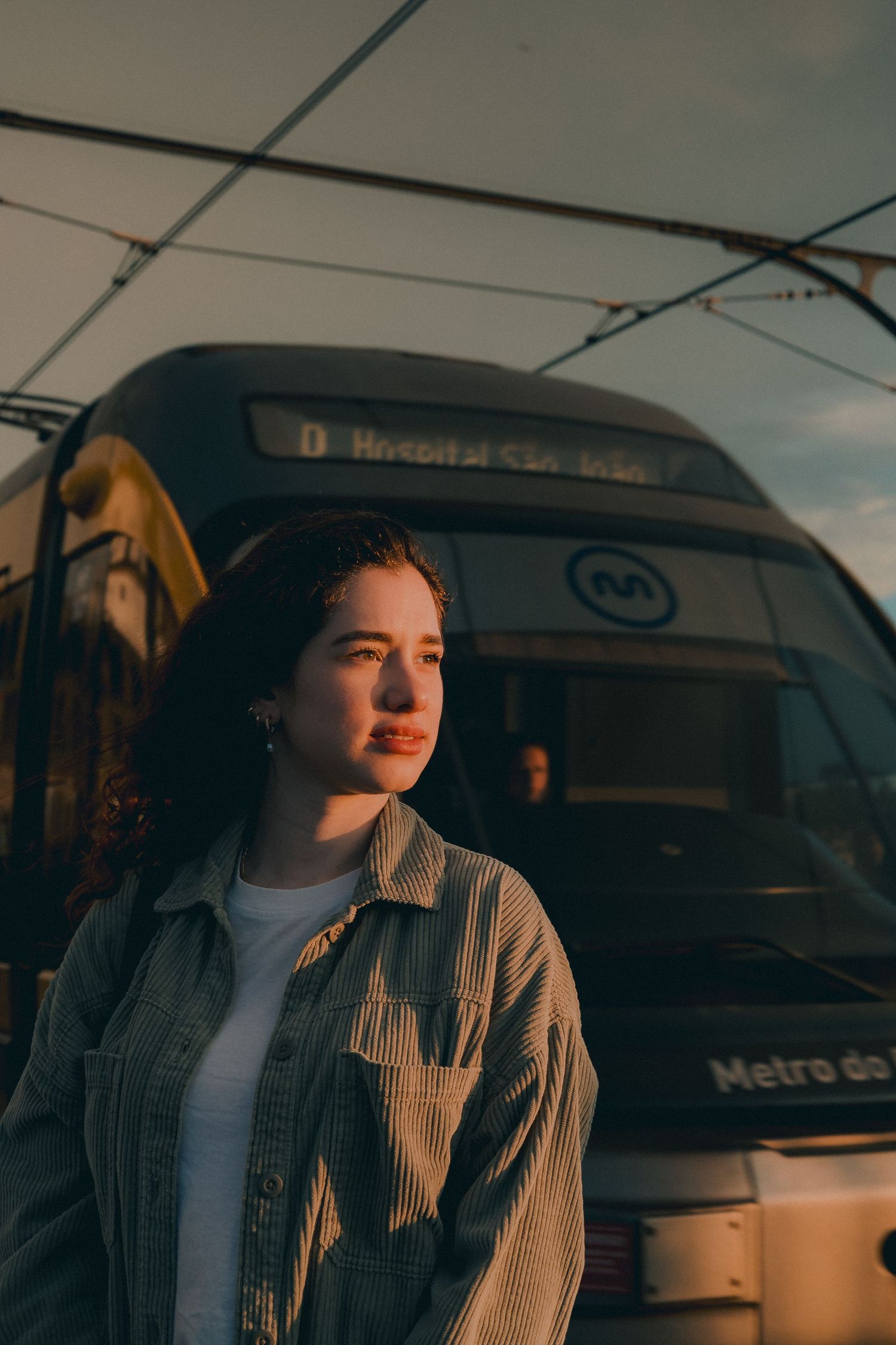 A person stands beside a public transit bus during sunset wearing casual attire.