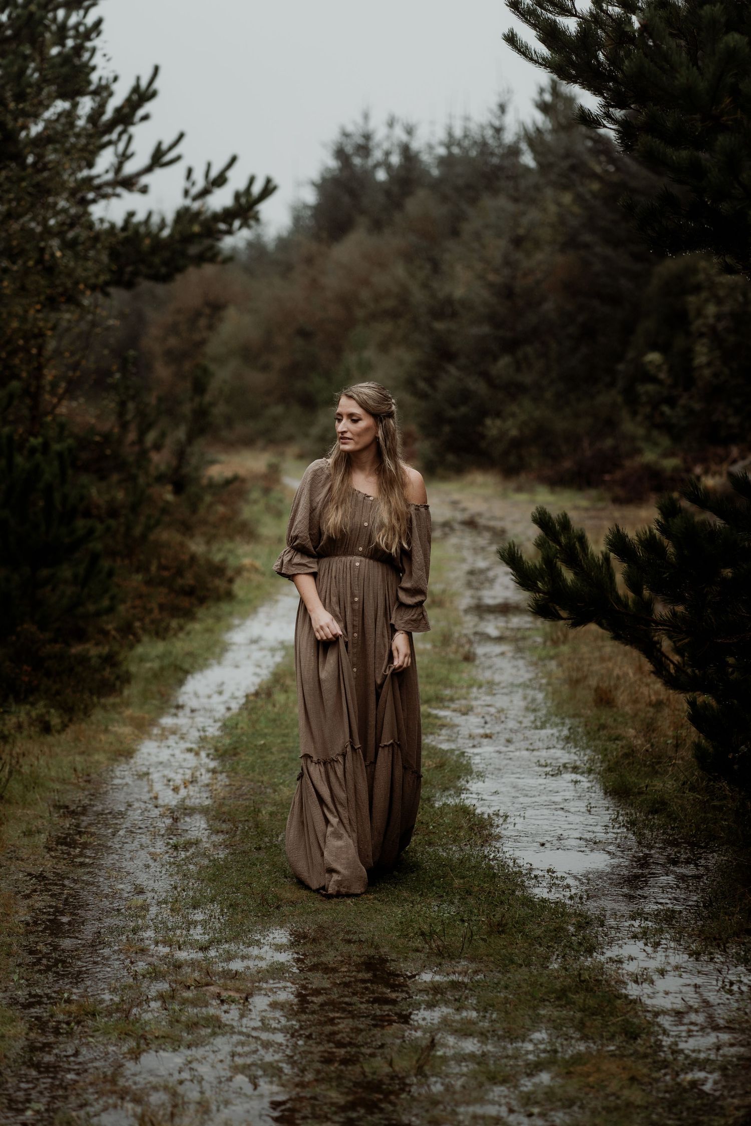 A flowing rust-colored dress billows dramatically against a moody waterfall backdrop in a romantic forest setting.