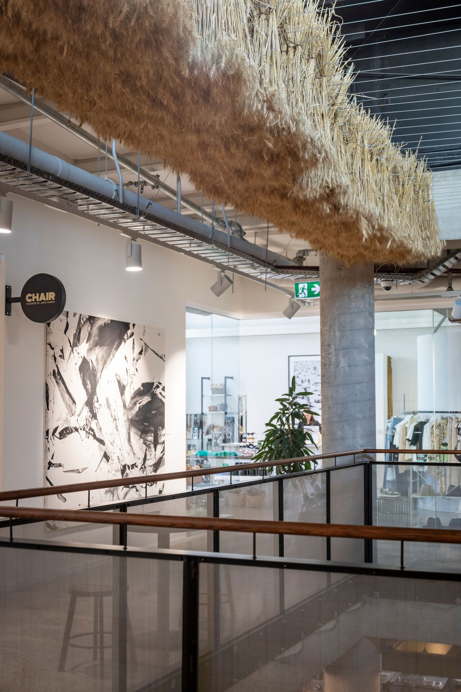 Indoor space with suspended straw ceiling installation above a gallery-like corridor.