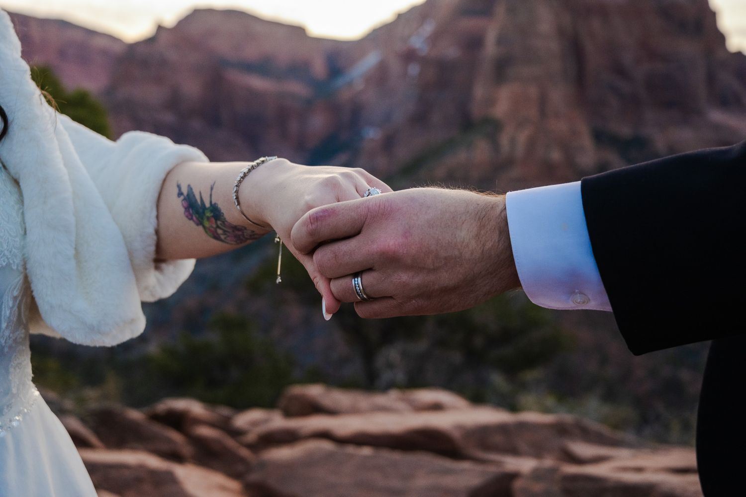 Close-up of bride and groom exchanging rings with stunning red rock canyon landscape in the background.