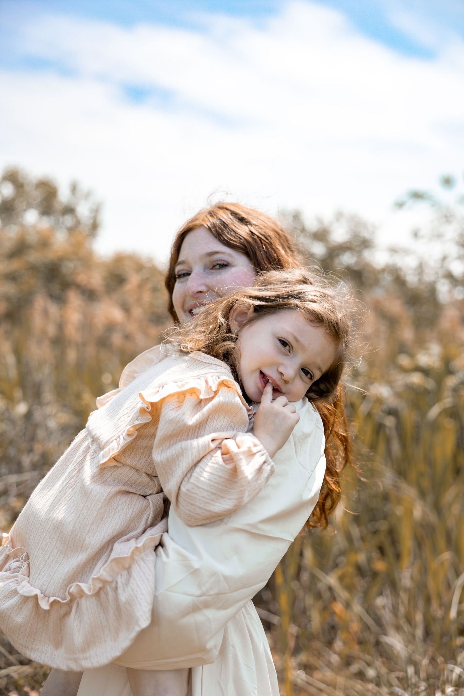 A joyful moment captured in a sun-drenched field with light cream-colored dresses and flowing hair in the breeze.