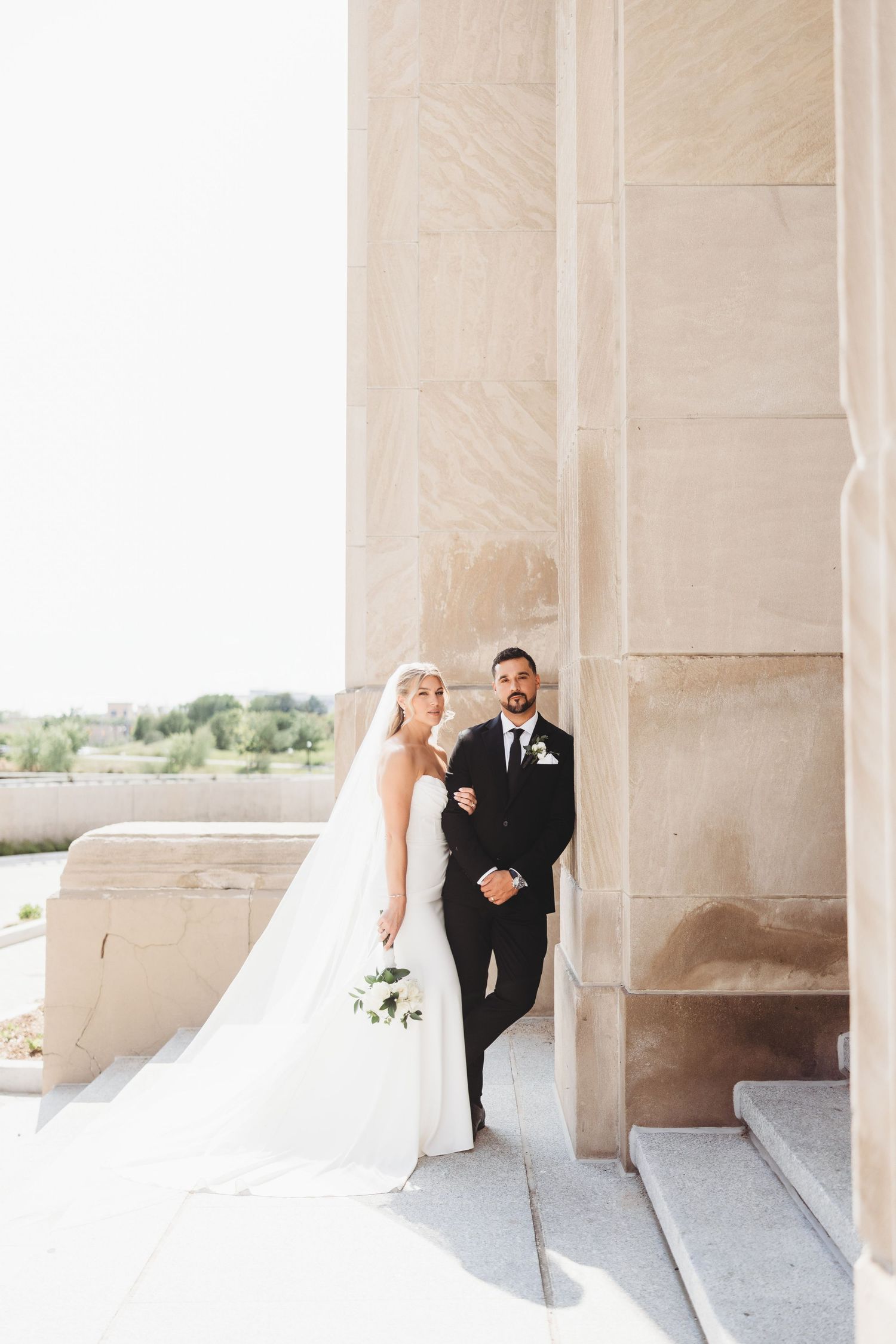 Wedding couple poses between dramatic stone columns with natural lighting. Grand Rapids Michigan