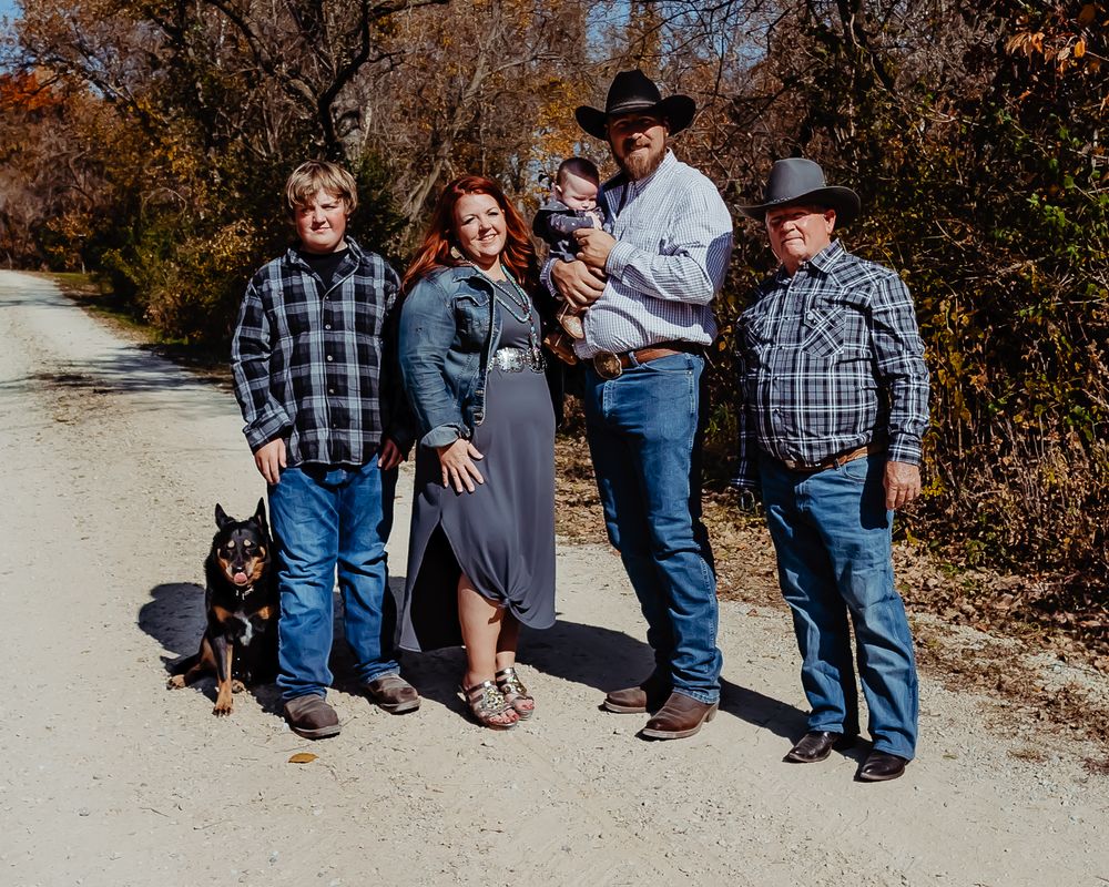 A group stands together on a dirt path with their dog during autumn, surrounded by fall foliage.