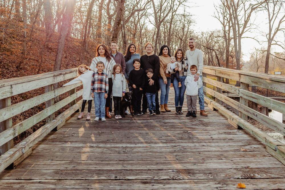 A group standing together on a wooden bridge in an autumn forest with sunlight filtering through the trees.