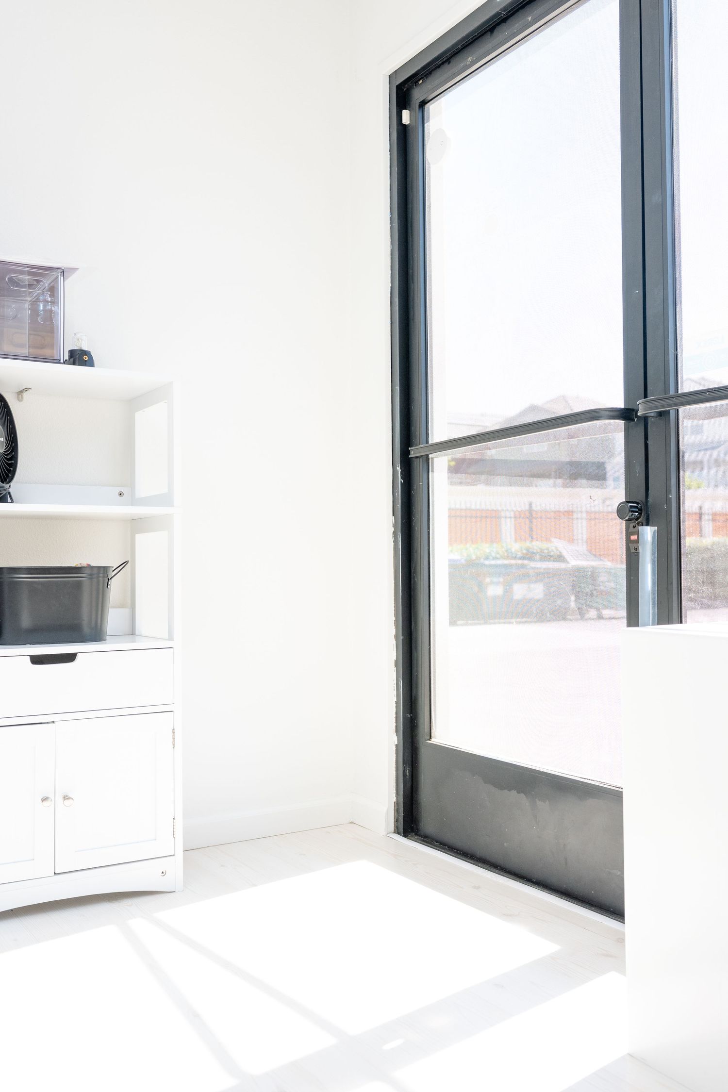 Modern white interior with large black-framed windows and white storage cabinet.