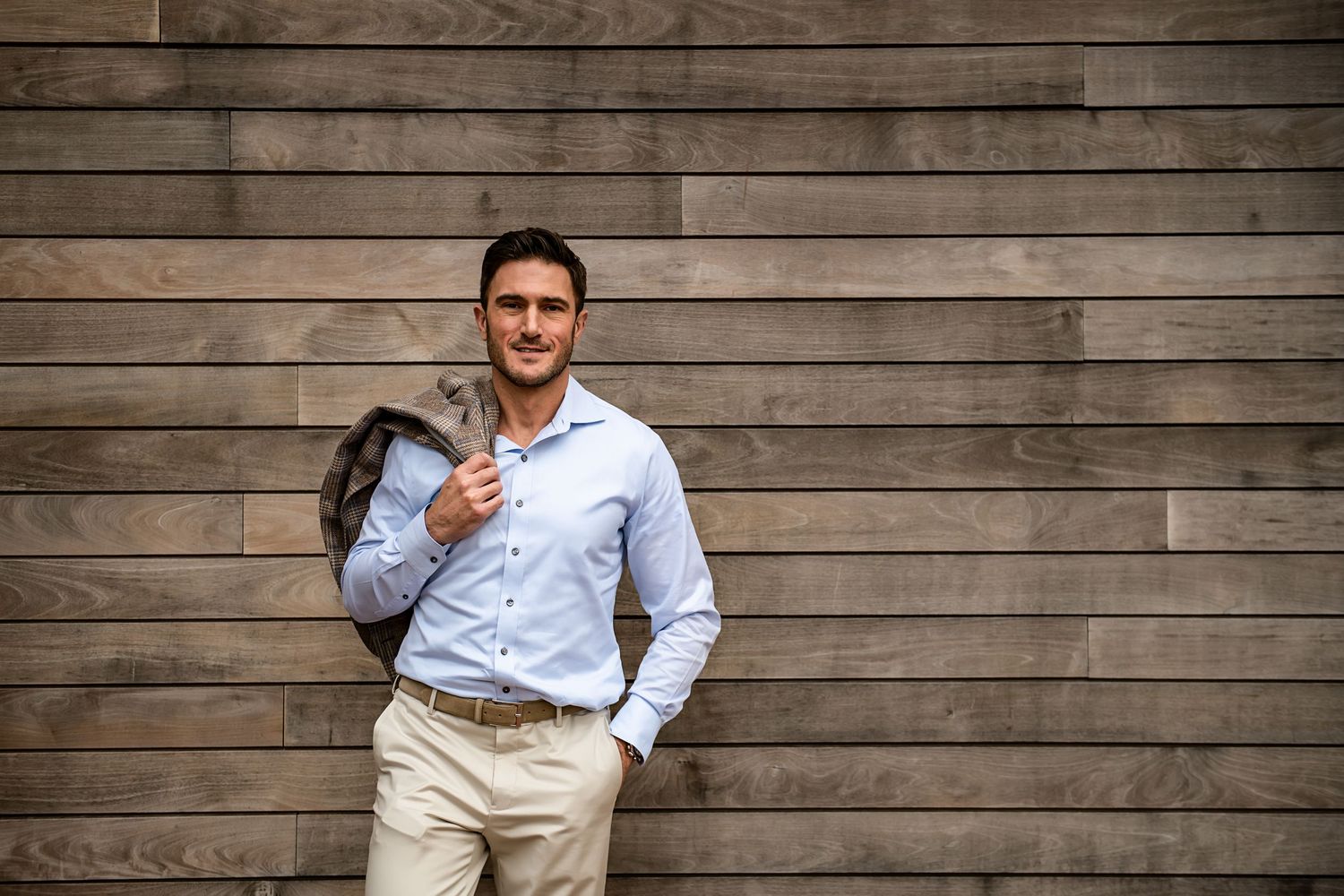 Casual portrait of well-dressed man leaning against wooden wall background.