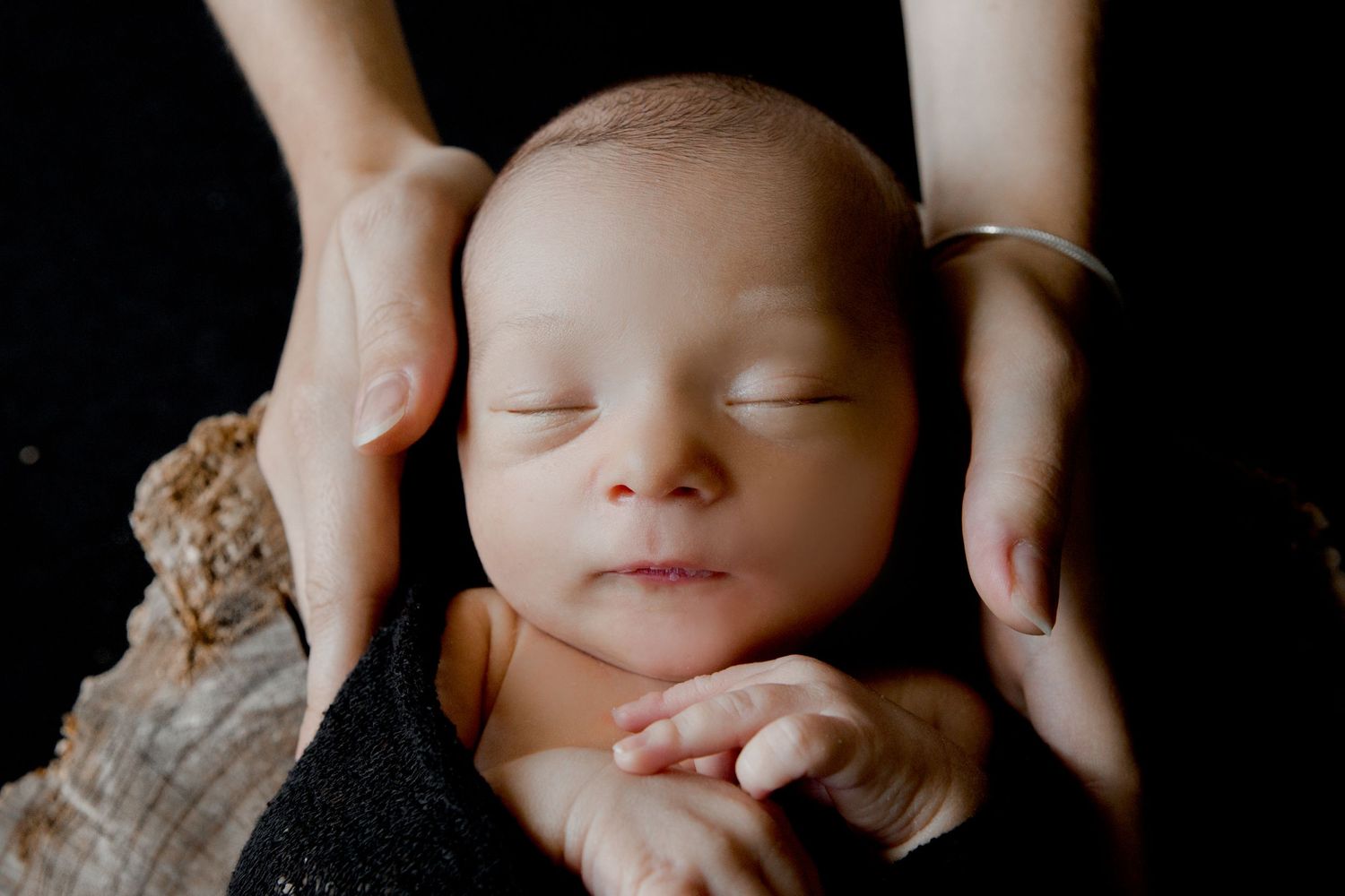 Close-up portrait of a peaceful sleeping newborn baby with hands gently cradling their head.