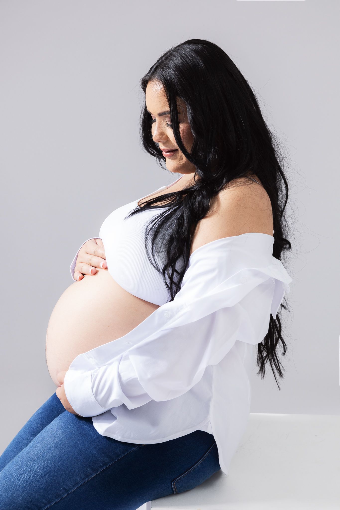 A pregnancy photoshoot series featuring an expectant mother in white top and jeans against a gray backdrop.