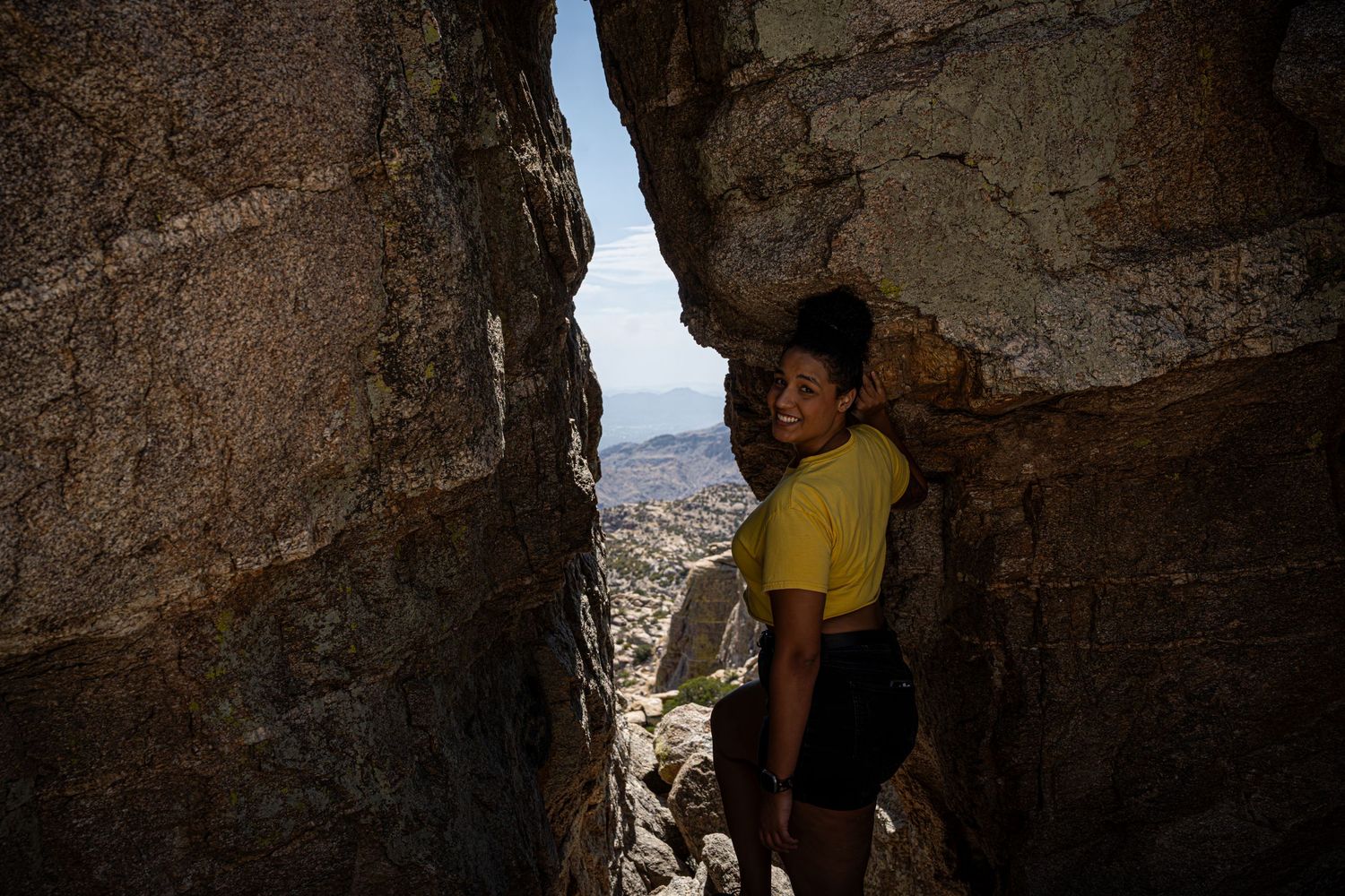 View through rocky cave opening showing arid mountain landscape.