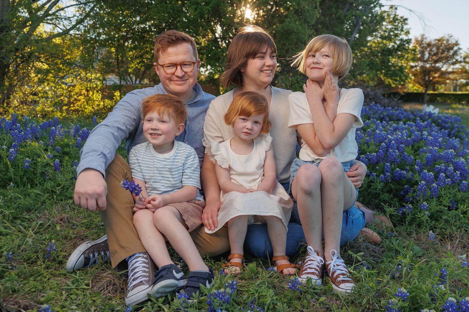 A family sits together among blooming bluebonnets in a sunlit field during golden hour.