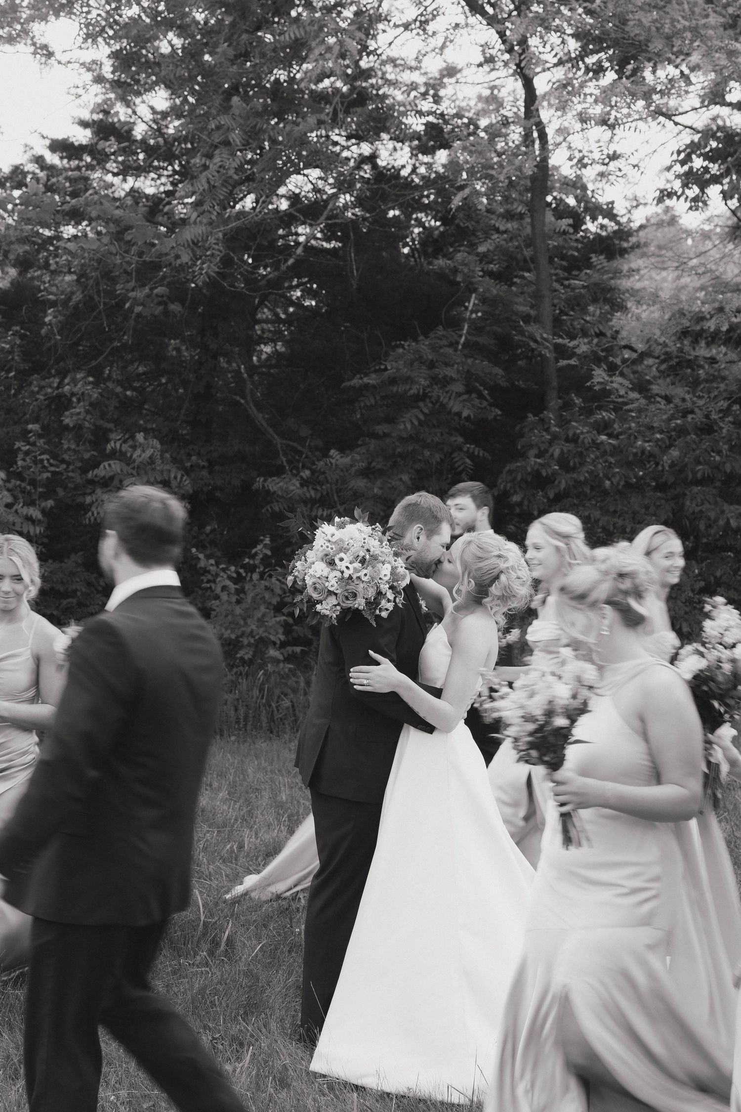 Wedding party stands in a garden setting with bride in white gown holding vibrant colorful bouquet.