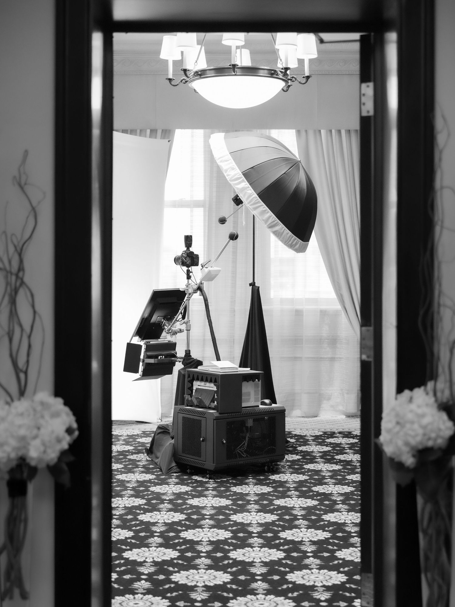 Classic photo booth photography studio setup with lights, tripod, umbrella reflector, and vintage equipment visible through doorway.