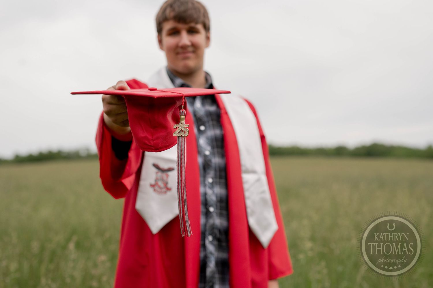 A person wearing a red raincoat and boots poses in a green grassy field against an overcast sky.