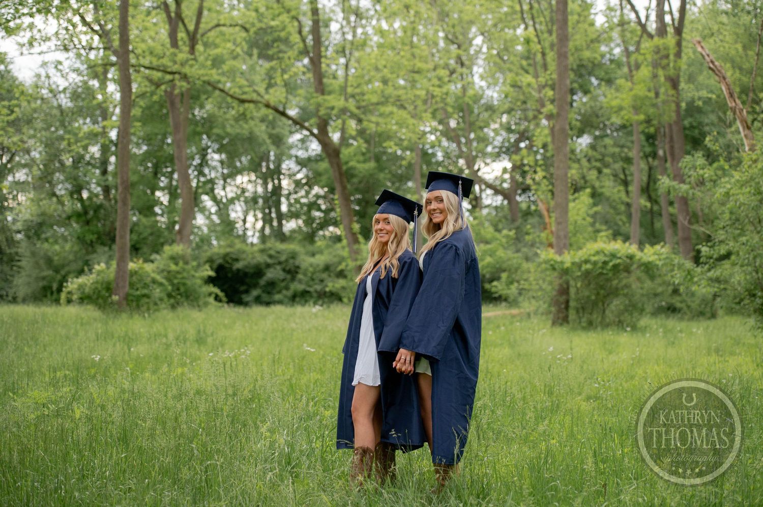 Two figures in white summer dresses hold hands while walking through a sunlit wooded meadow in black and white.