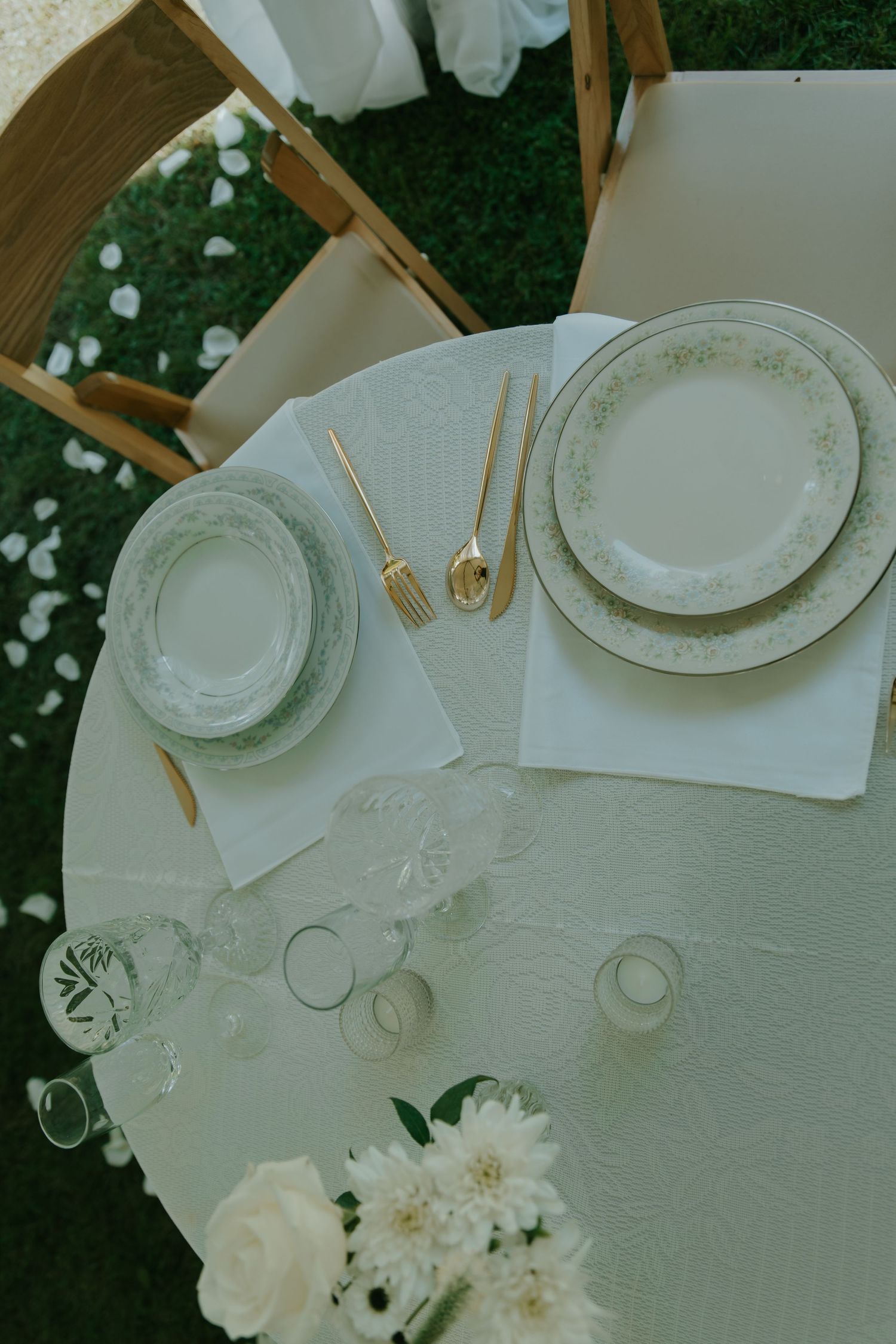 Elegant place setting with vintage plates and gold cutlery at outdoor wedding reception.