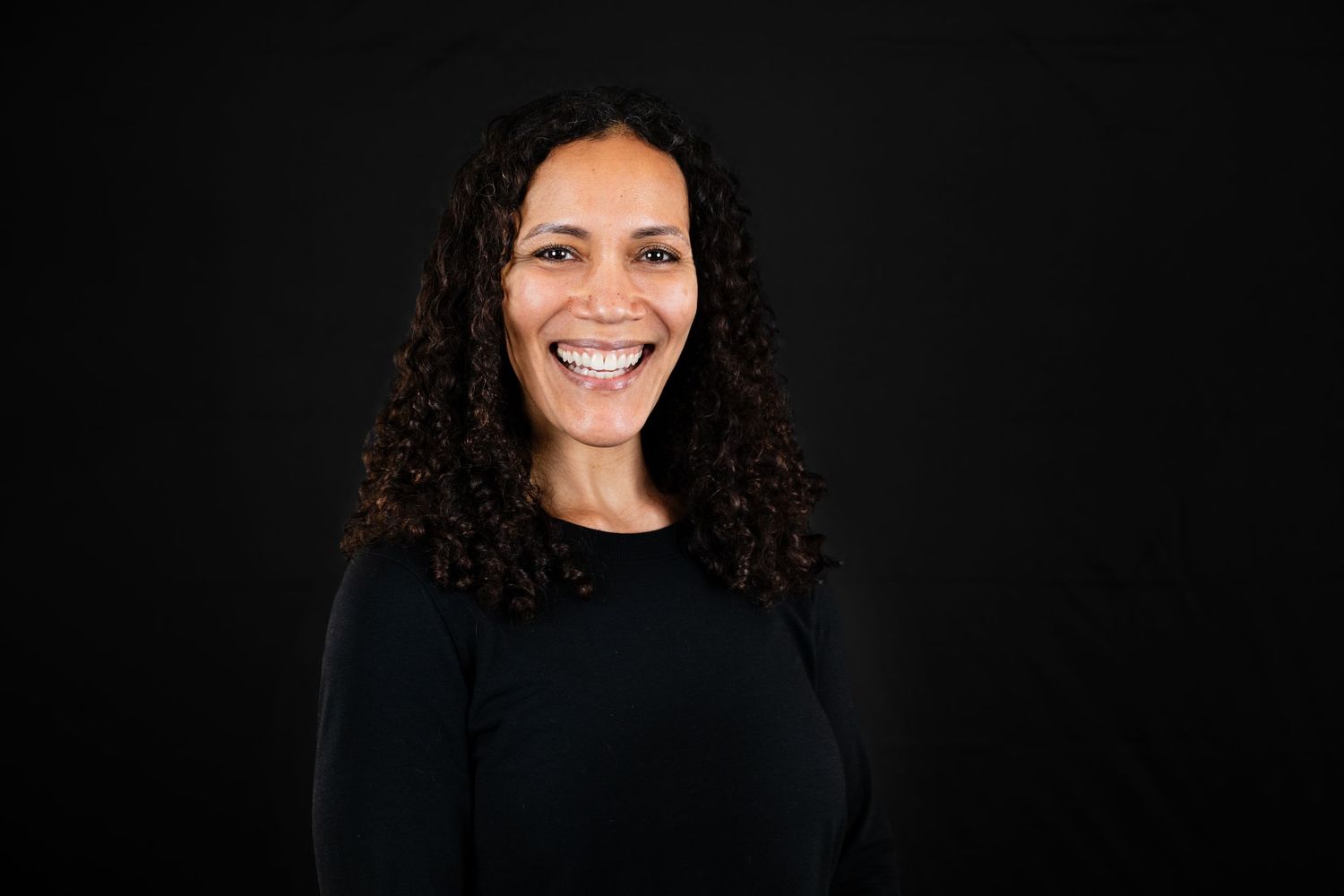 A person in a black top smiling against a dark background in a series of professional headshot poses.