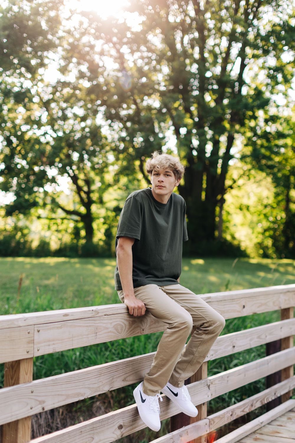 Athletic figure sits casually posed along a wooden fence in late afternoon sunlight.