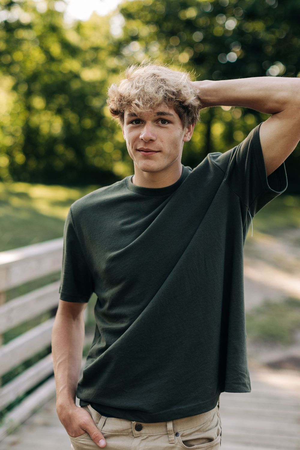 A casual outdoor portrait shot of someone in a dark t-shirt with curly hair against a natural green background.