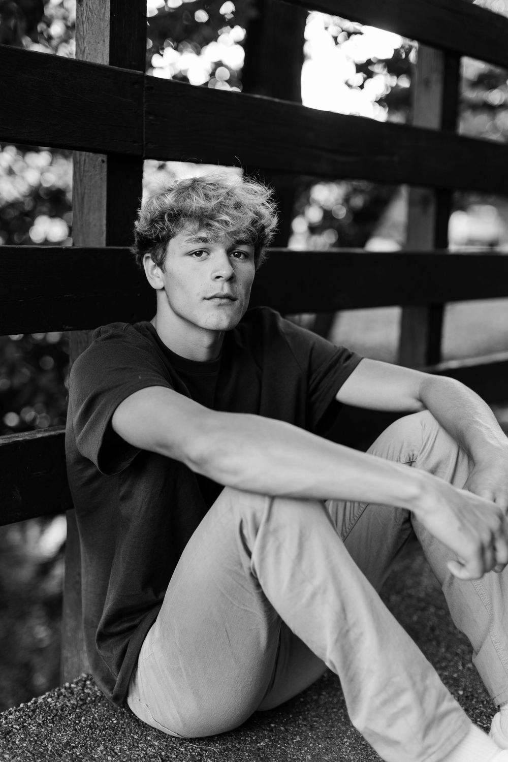 Moody black and white portrait captured through wooden fence slats.