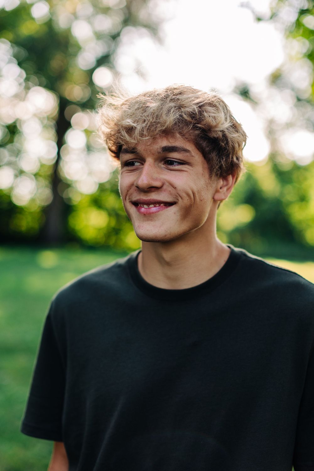 Close up portrait with soft bokeh background showing a warm smile and casual black t-shirt.