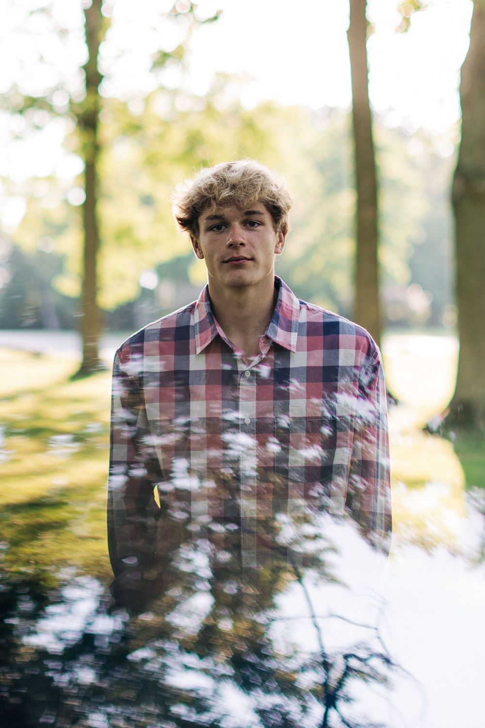 Double exposure portrait merging face with forest scenery in soft natural light.