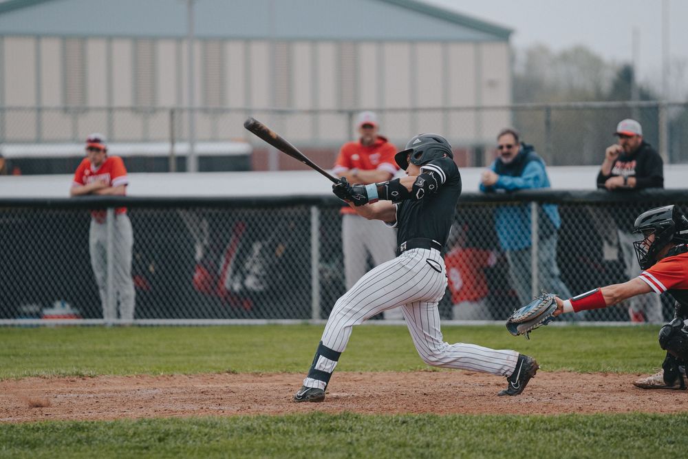 Sports Photography of baseball batter in black uniform swinging at pitch during game with spectators watching  - Warsaw, Indiana