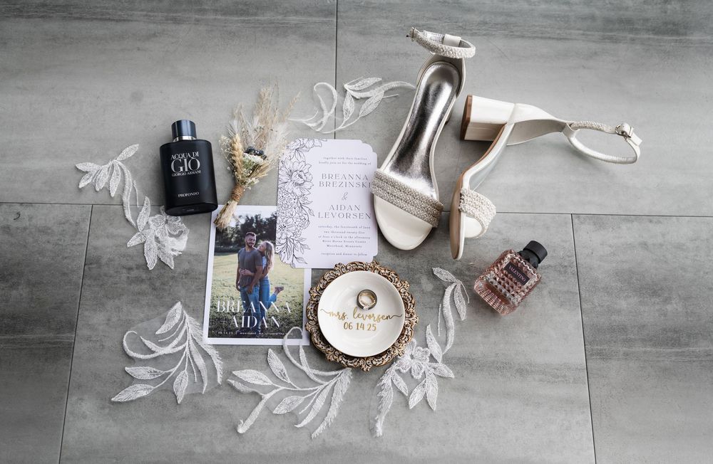 Wedding detail flatlay featuring white heels, perfume bottles, and delicate decor on gray flooring.