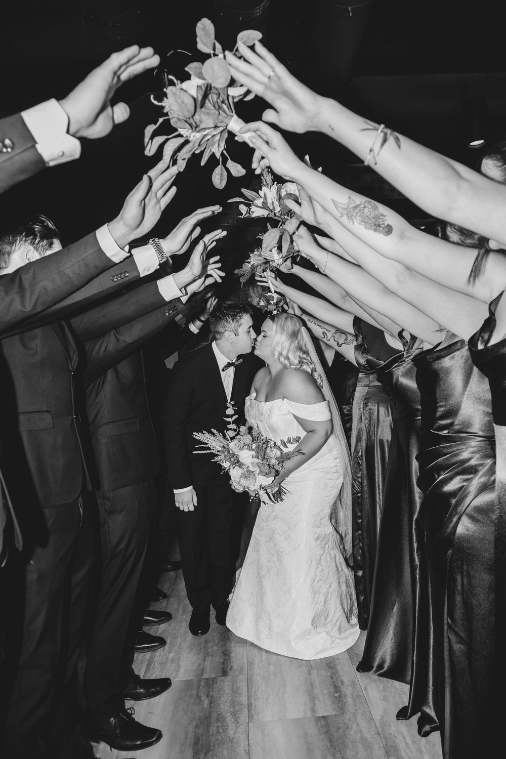 Black and white wedding reception photos show couple dancing with guests reaching towards them on the dance floor.