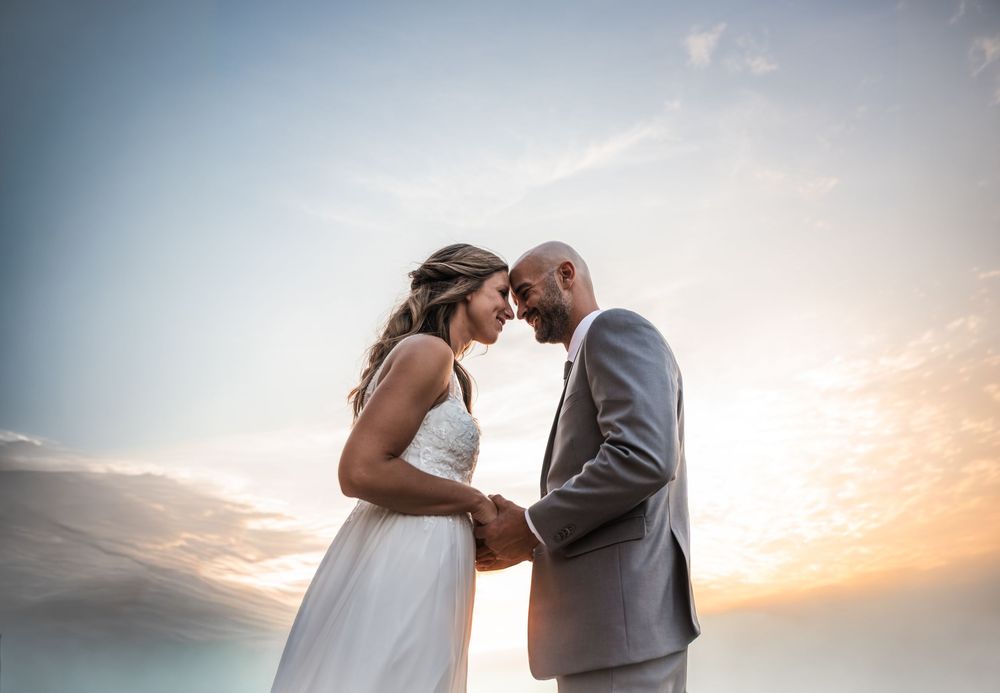Couple in wedding attire sharing a romantic moment at sunset by the ocean.