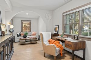 Modern Mediterranean style study with arched doorway, light wood floors, neutral tones and orange accents. Real estate photography.