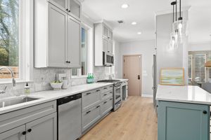 Modern white and gray kitchen, light hardwood floors, pendant lights, and sage green island features marble countertops. Real estate photo.