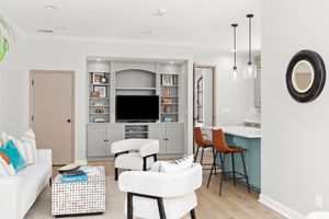 Modern light-filled interior of an open-concept apartment with grey and white decor featuring a kitchen and living space. Real estate photo.