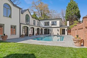 Modern white stucco mansion with arched windows features a backyard swimming pool and manicured green lawn.