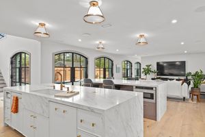 Bright modern kitchen, white cabinets, pendant lights, stainless appliances and hardwood floors in open concept design. Real estate photo.