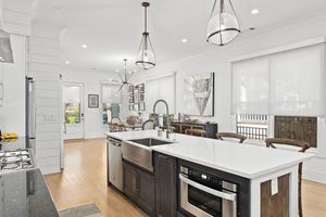 Modern white kitchen with dark lower cabinets, quartz countertops, and track lighting showcases open concept design. Real estate photo.