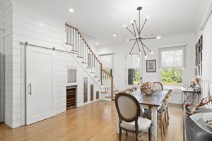 Bright white dining room with modern sputnik chandelier, wood floors and elegant stairs featuring under-staircase storage. Real estate photo