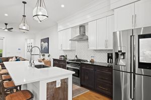 Modern kitchen showcases white upper cabinets, dark base cabinets, stainless steel smart appliances with pendant lights. Real estate photo.