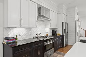 Modern kitchen with white marble backsplash, dark cabinets, stainless appliances and hardwood floors in panoramic view. Real estate photo.