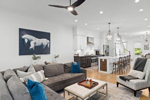 Modern open concept living room, grey sectional sofa, blue accents, and contemporary horse artwork above the couch. Real estate photography.