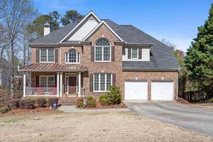 Large two-story brick colonial house with white trim, arched windows, and double garage in suburban setting. Real estate photography.