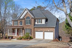 Large two-story brick suburban home with arched windows, double garage, and covered front porch on a wooded lot. Real estate photography.