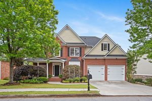 Beautiful two-story beige and brick suburban home with white trim, double garage, and manicured landscaping. Real estate photography.