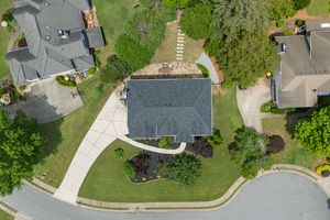 Aerial view of a suburban house with dark gray roof and well-maintained lawn on a corner lot surrounded by trees. Real estate photography.