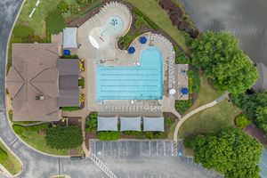 Aerial view of a community swimming pool complex, lap lanes and curved leisure pool surrounded by trees and parking lot. Real estate photo.