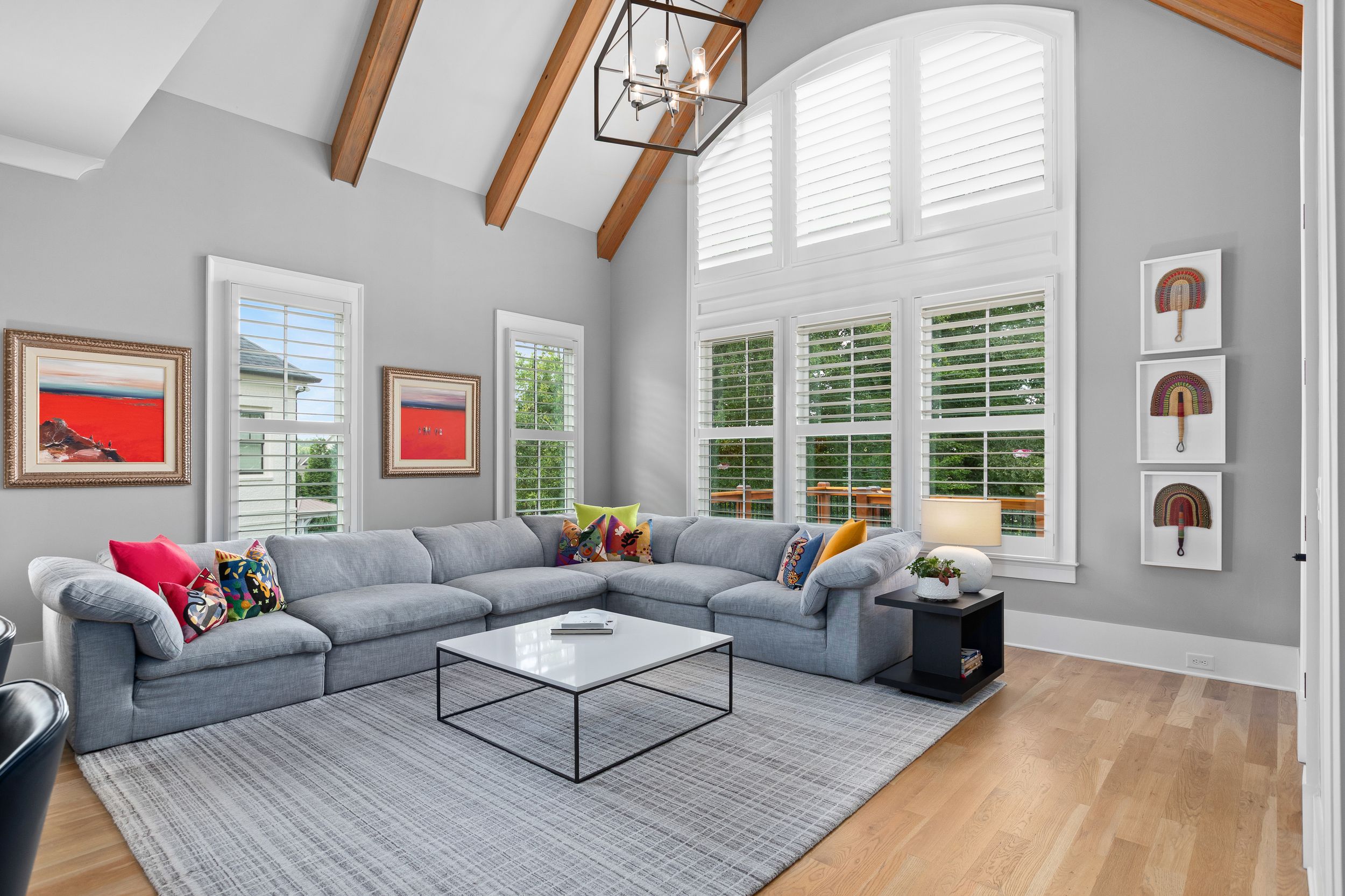 Modern living room with vaulted ceiling, gray sectional sofa, hardwood floors and red artwork on light gray walls. Real estate photography.
